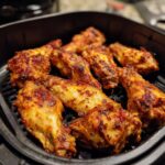 Close-up shot of golden brown, crispy air fryer chicken wings arranged in an air fryer basket.