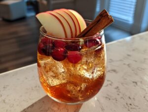 A festive Apple Cider Long Island Iced Tea cocktail with ice, cranberries, apple slices, and a cinnamon stick.