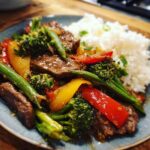 A plate of vibrant beef stir fry with tender beef strips, broccoli, bell peppers, and green beans, served with fluffy white rice.