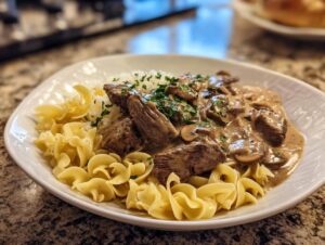 A close-up of a white plate filled with beef stroganoff, mushrooms, creamy sauce, white rice, and egg noodles, garnished with parsley.