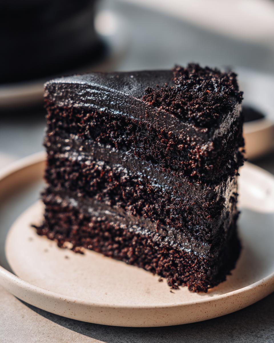 A decadent slice of Black velvet cake with layers of dark chocolate cake and frosting, served on a plate.