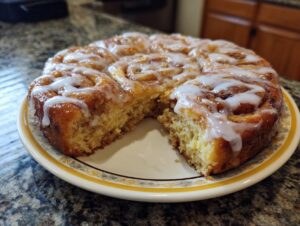 A close-up of a freshly baked cinnamon roll casserole, drizzled with white glaze, on a decorative plate.