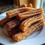 A close-up shot of a pile of freshly made churros, coated in cinnamon sugar.