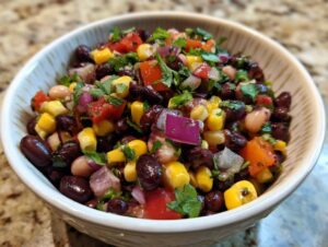 A close-up of a bowl filled with vibrant Cowboy Caviar, featuring black beans, corn, tomatoes, red onion, and cilantro.