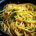 Close-up of spaghetti tossed in a creamy lemon sauce, garnished with fresh parsley and lemon zest.