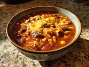 A close-up of a bowl of Crockpot Chicken Enchilada Soup topped with melted cheese, corn, and black beans.