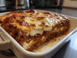 A close-up of a freshly baked Easy Lasagna with Ricotta in a white baking dish, showing layers of pasta, meat sauce, and creamy ricotta cheese.