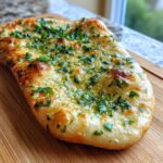 Close-up of a golden-brown garlic naan bread topped with melted butter and fresh chopped parsley.