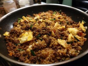 Close-up of delicious ground beef fried rice with scrambled eggs and green onions in a skillet.