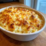 A close-up of a golden brown, bubbly hashbrown casserole in a white baking dish, ready to serve.