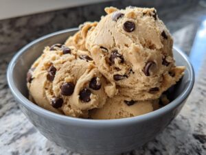 Close-up of a bowl filled with scoops of creamy high protein cookie dough studded with chocolate chips.