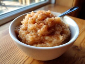 A close-up of a white bowl filled with chunky homemade applesauce, lightly dusted with cinnamon.