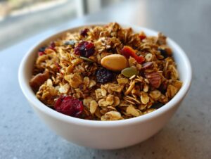 A close-up shot of a white bowl filled with delicious homemade granola, featuring oats, nuts, seeds, and dried fruit.