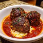 Close-up of three juicy mozzarella stuffed meatballs in a rich tomato sauce, garnished with fresh herbs.