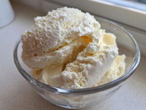 A close-up of creamy, pale yellow protein ice cream scooped into a clear glass bowl.