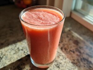 A tall glass filled with a vibrant pink Strawberry Mango Smoothie, topped with a light foam.