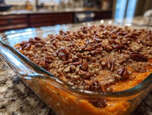 Close-up of a freshly baked sweet potato casserole topped with crunchy pecans and a crumble topping in a glass baking dish.