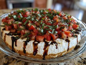 A round, layered bruschetta dip featuring a creamy white base, topped with diced tomatoes, fresh basil, and drizzled with balsamic glaze.