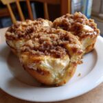 Three freshly baked apple crumble cheesecake buns with creamy filling and streusel topping on a white plate.