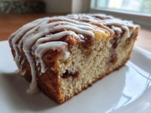 Close-up of a moist slice of apple fritter bread topped with thick white vanilla glaze dripping down the side.