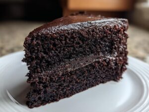 A rich slice of black velvet halloween cake with dark chocolate frosting on a white plate.