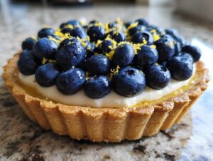 A close-up view of a delicious blueberry mascarpone tart, generously topped with fresh blueberries and lemon zest.