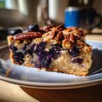 A close-up of a slice of rustic Blueberry Pecan Cobbler, topped with whole pecans and fresh blueberries.