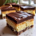 Close-up of a layered Boston Cream Pie Fudge bar, featuring a chocolate crust, creamy filling, caramel, and chocolate ganache topping.