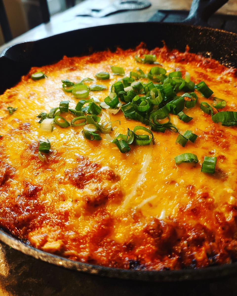 Close-up of bubbling hot buffalo chicken dip topped with melted cheese and green onions in a cast iron skillet.