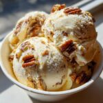 Close-up of creamy butter pecan ice cream scoops in a white bowl, generously studded with toasted pecans.