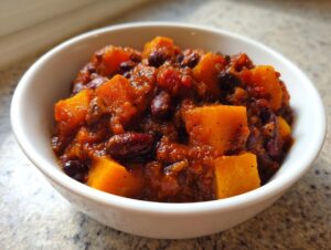 Close-up of a hearty serving of butternut squash chili, featuring large orange chunks of squash and dark red kidney beans in a rich sauce.