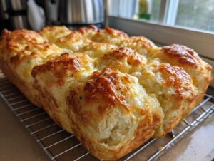 A golden-brown loaf of pull-apart cheese garlic rolls, baked to perfection and cooling on a wire rack.