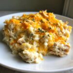A close-up serving of creamy, cheesy chicken and rice casserole topped with melted cheddar and fresh thyme.
