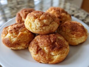 A close-up of several chewy snickerdoodle cookies piled on a white plate, dusted with cinnamon sugar.