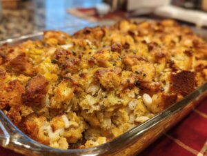 Close-up of a golden brown chicken stuffing casserole, baked in a glass dish, with visible chunks of bread and chicken.