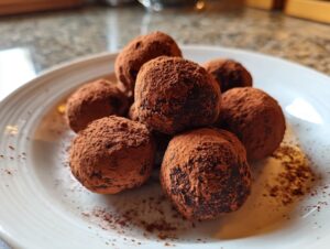A pile of rich chocolate ricotta truffles generously dusted with cocoa powder on a white plate.