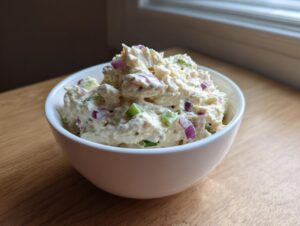 A white bowl filled with creamy cottage cheese chicken salad mixed with visible chunks of red onion and celery.