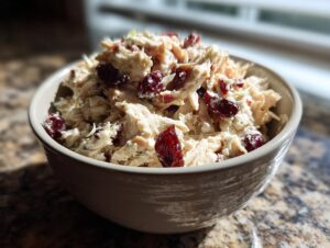 A close-up of a bowl filled with creamy Cranberry Apple Chicken Salad, featuring shredded chicken and dried cranberries.