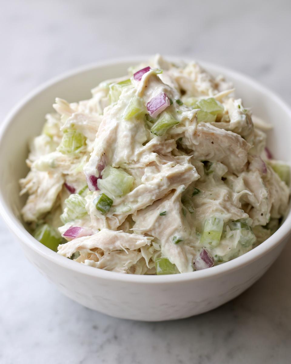 A close-up shot of creamy avocado chicken salad mixed with celery and red onion, served in a white bowl.