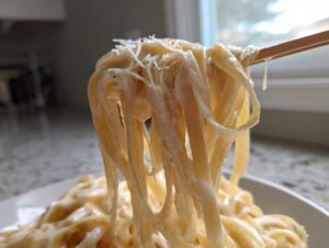 Close-up of fettuccine noodles coated in creamy homemade alfredo sauce being lifted by chopsticks.