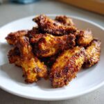 A close-up of a pile of golden-brown, crispy baked chicken wings served on a white plate.