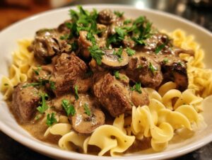 A close-up of Crock Pot Beef Stroganoff served over egg noodles, garnished with fresh parsley.