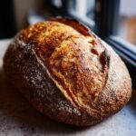 A beautiful, golden-brown loaf of crusty Italian bread with a scored top, resting on a speckled countertop.