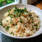 A white bowl filled with fluffy rice pilaf recipe, mixed with toasted vermicelli and garnished with fresh chopped parsley.