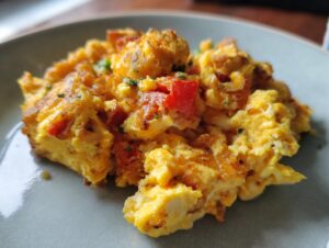 Close-up of fluffy scrambled eggs with chunks of tomato and chopped herbs on a gray plate.