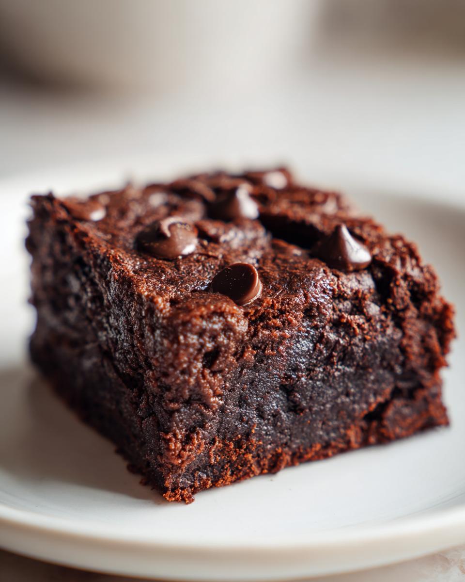 A close-up of a fudgy sweet potato brownie topped with chocolate chips on a white plate.