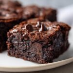 Close-up of a fudgy sweet potato brownie topped with chocolate chips on a white plate.