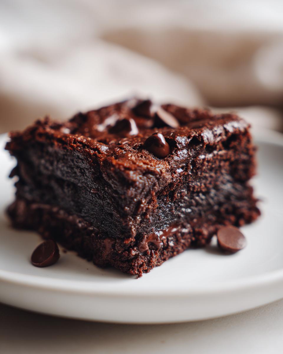 A close-up of a fudgy sweet potato brownie topped with chocolate chips on a white plate.