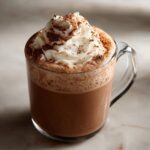 A festive mug of Gingerbread Hot Chocolate topped with creamy whipped cream and a dusting of cocoa powder.