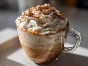 A festive mug of Gingerbread Hot Chocolate topped with whipped cream and a dusting of cinnamon.